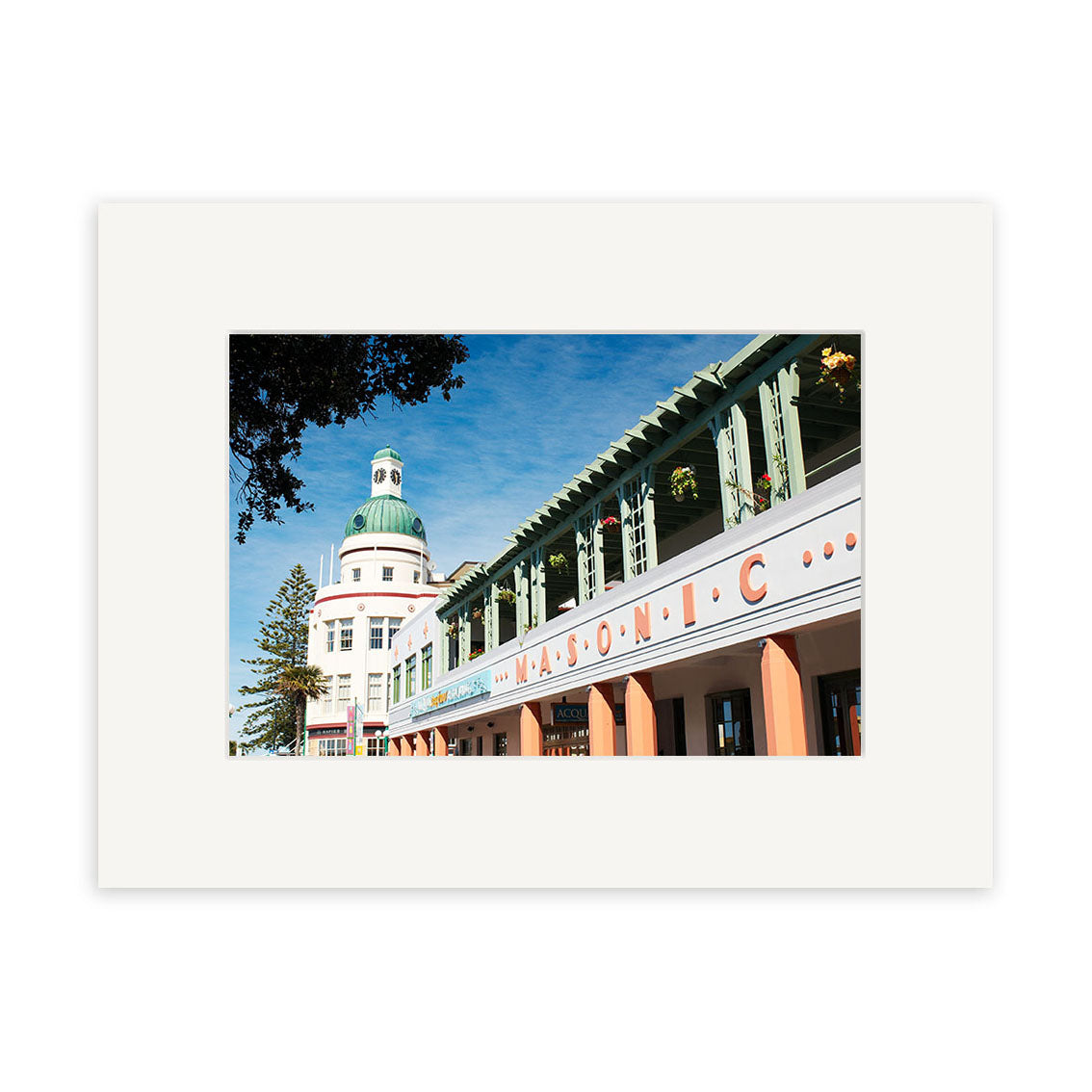 A photo of the Masonic - RP146 building in New Zealand, featuring Art Deco design and pastel tones against a blue sky, with trees and a green-domed tower—ideal for photographic prints on archival quality matte paper.