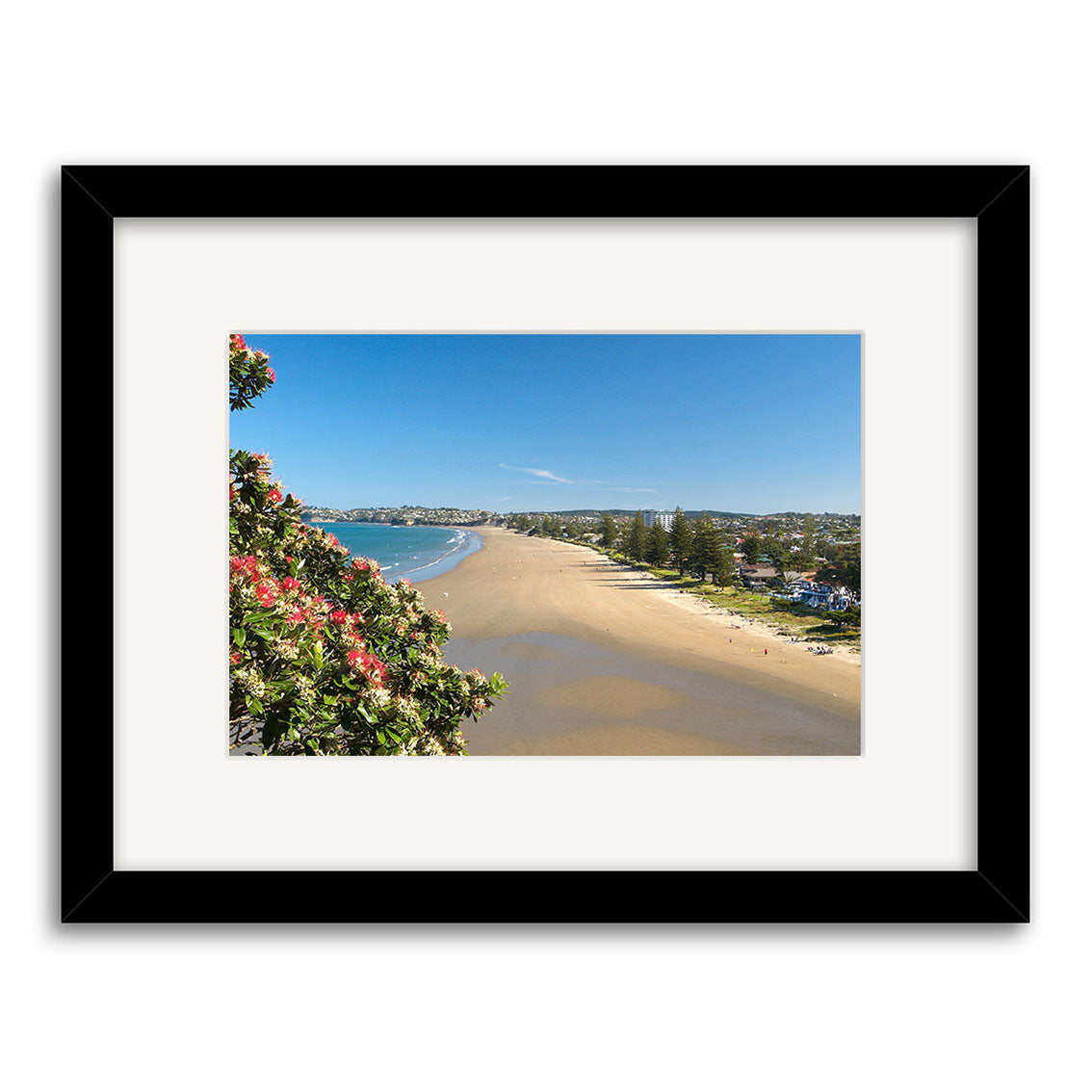Orewa - RP148: A framed photographic print of a wide sandy New Zealand beach with flowers, greenery, and distant shoreline buildings under a blue sky. Printed on archival quality matte paper for lasting beauty.