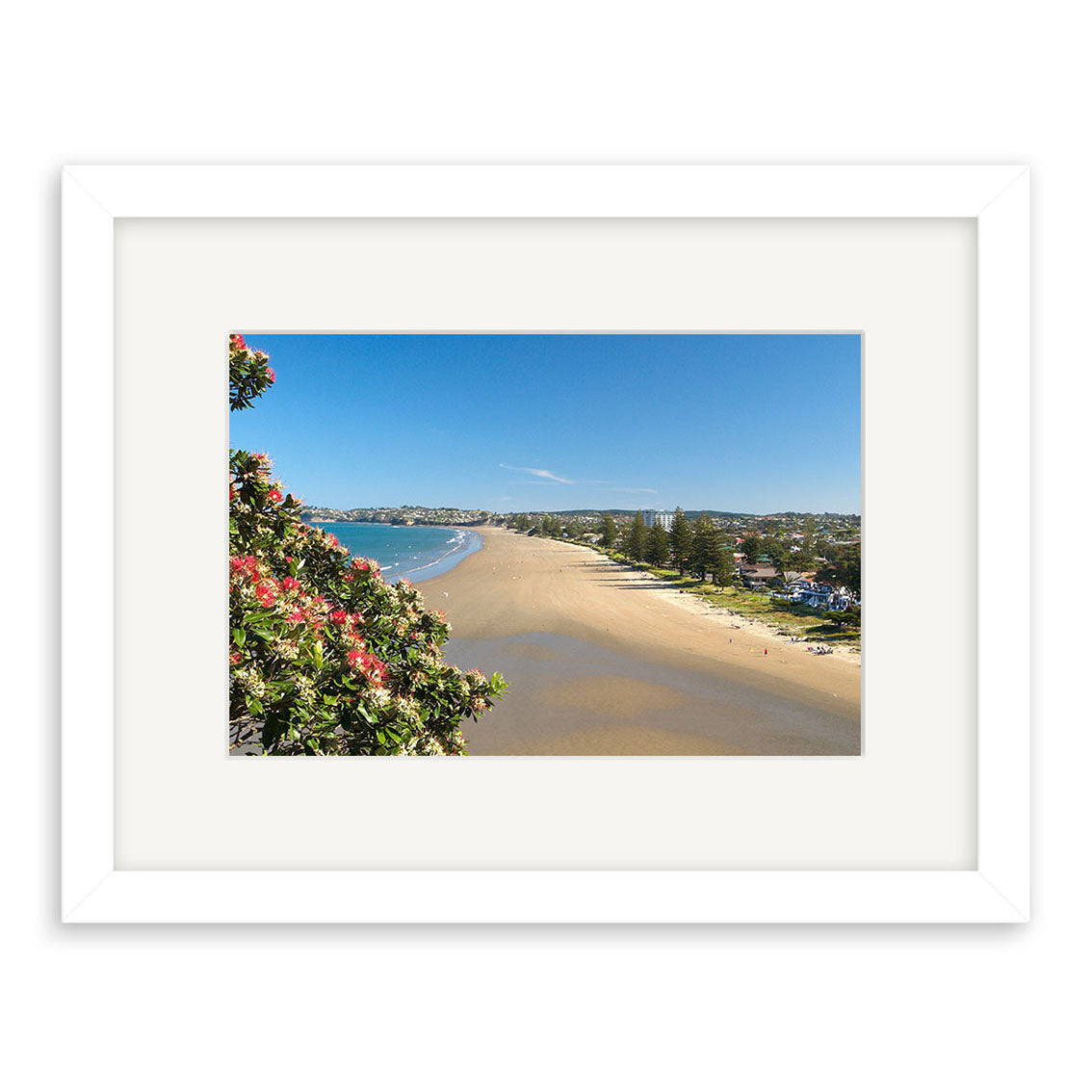 Orewa - RP148: A framed photo on archival matte paper depicting a sandy New Zealand beach with calm water, people walking along the shore, flowering plants in the foreground, and distant buildings under a clear blue sky.