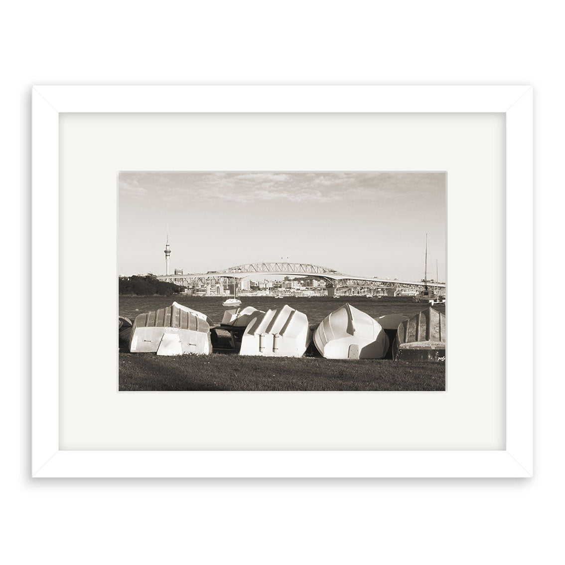 Little Shoal Bay – RP149 is a framed black-and-white photo on archival matte paper, depicting small boats upside down on grass in New Zealand with a large bridge and tall tower in the partly cloudy background.