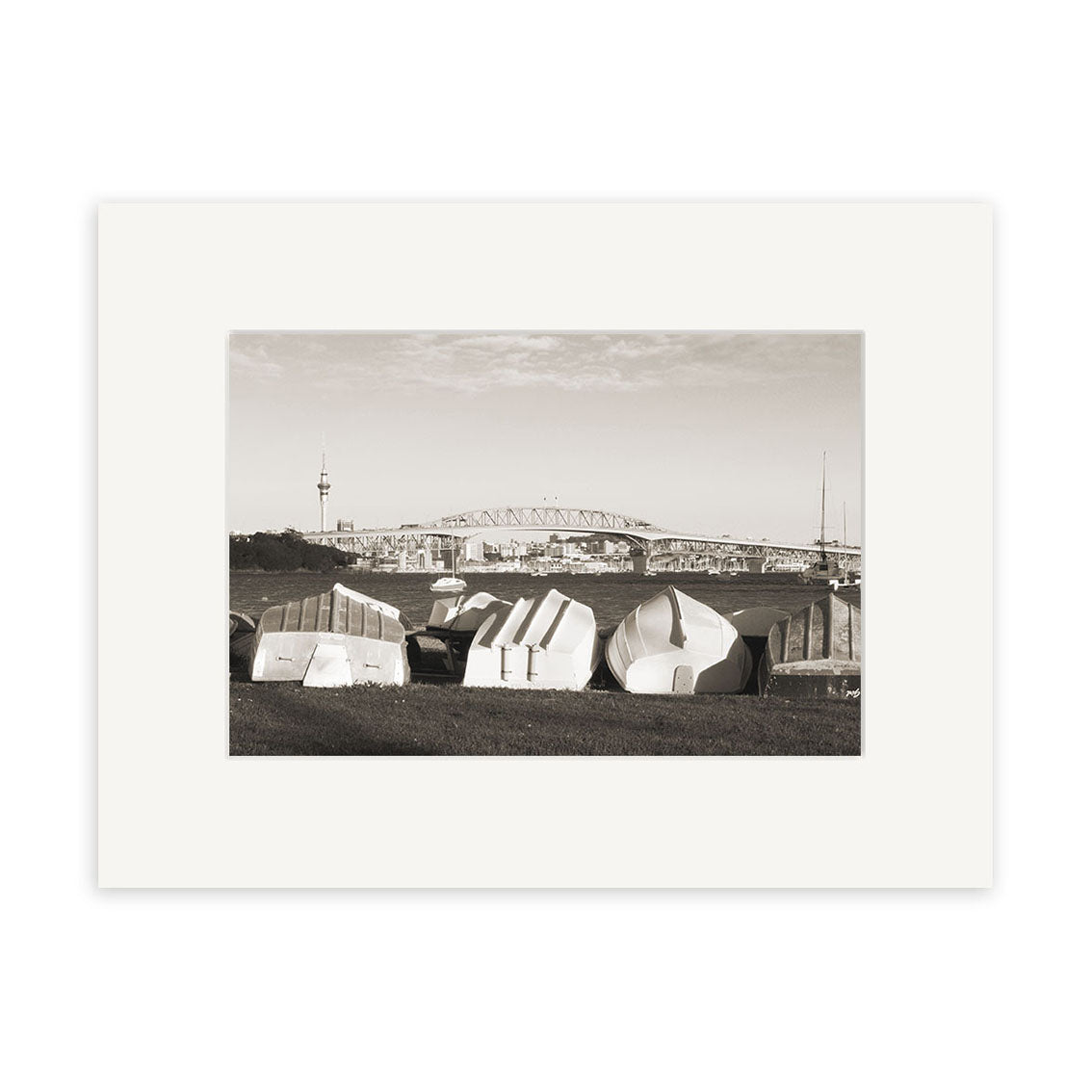 Little Shoal Bay - RP149: Black-and-white photo of upside-down boats on grass in New Zealand, with a bridge and tall tower in the background under a partly cloudy sky. Available as archival quality matte paper print.