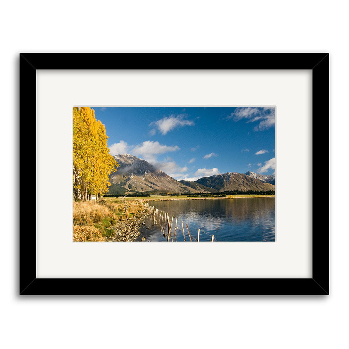 Lake Grasmere - RP153: Archival-quality framed photographic print showcasing New Zealand’s serene beauty—a calm lake with rocky shore, golden trees on the left, distant mountains, and a vivid blue sky with scattered clouds.