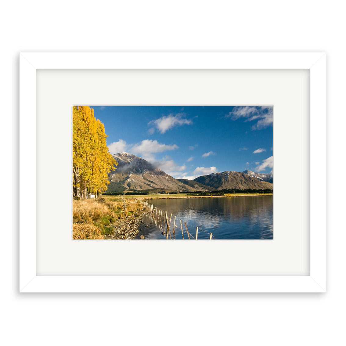 Lake Grasmere - RP153: This framed archival print features a stunning New Zealand landscape—still lake waters, a rocky shore, yellow-leaved trees on the left, and mountains with clouds—ensuring lasting beauty for your space.