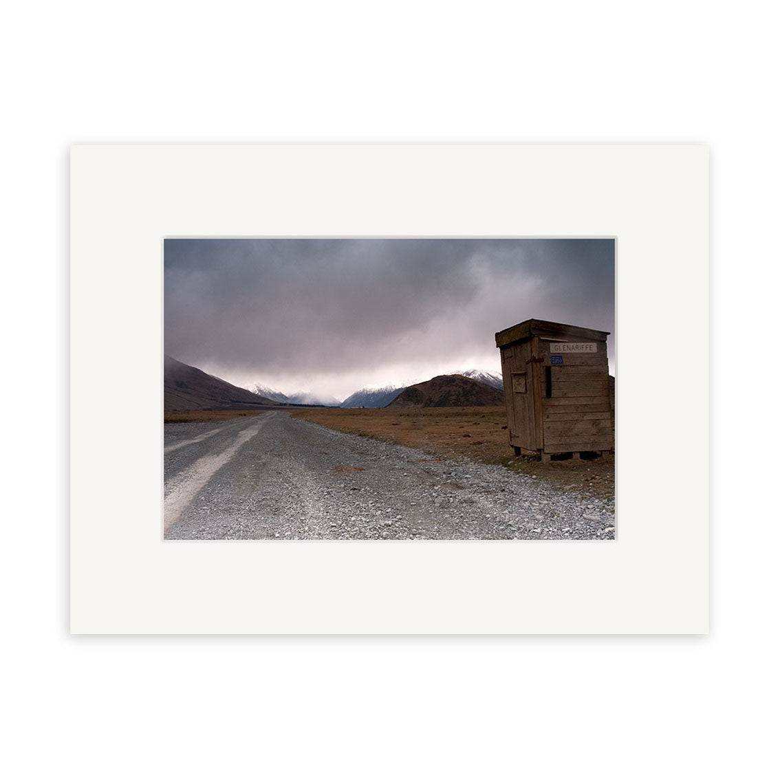 A gravel road leads toward distant hills under a cloudy New Zealand sky, passing a wooden shack labeled Mr. Bureau—available as Glenariffe - RP155 photographic prints on archival quality matte paper.