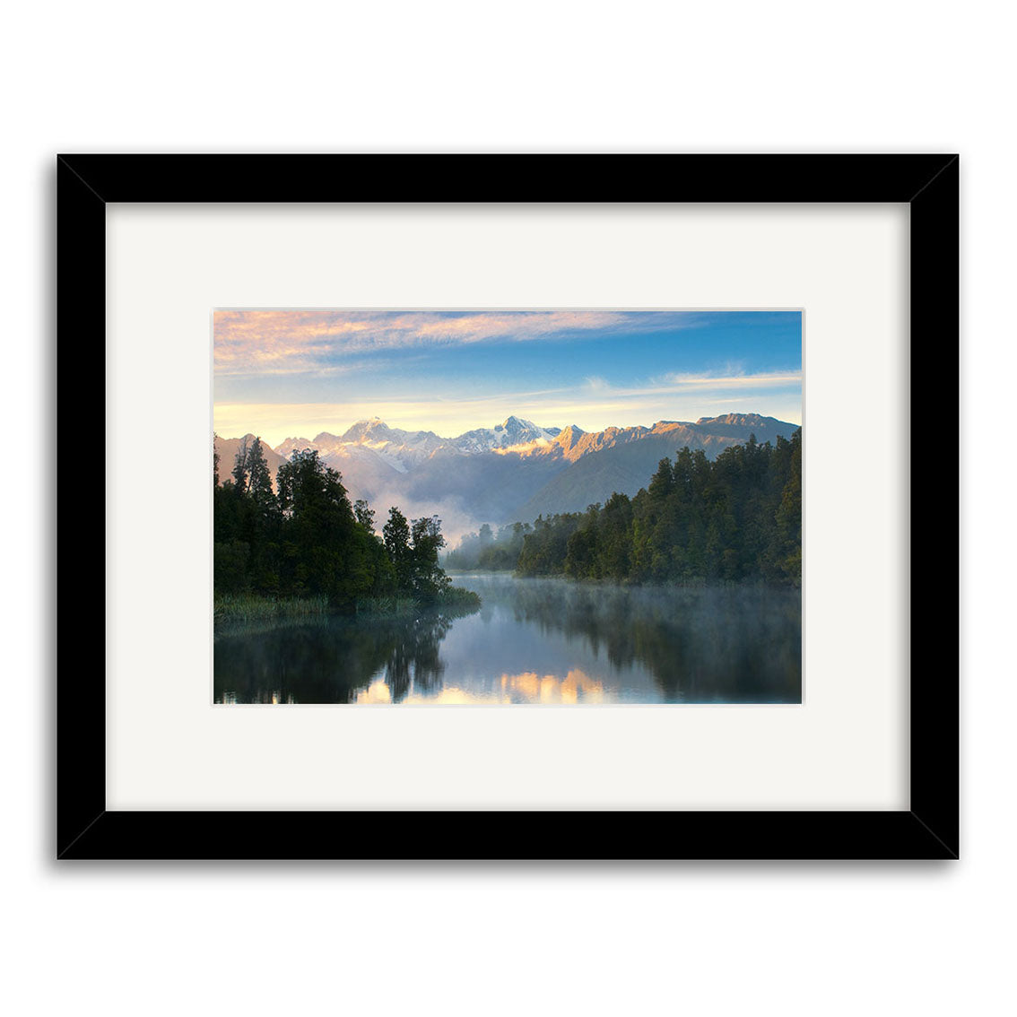 Framed photographic print titled Lake Matheson - RP157 shows a calm New Zealand lake mirroring trees and distant snow-capped mountains under a cloudy sky, softly illuminated. Image by Reuben Price.