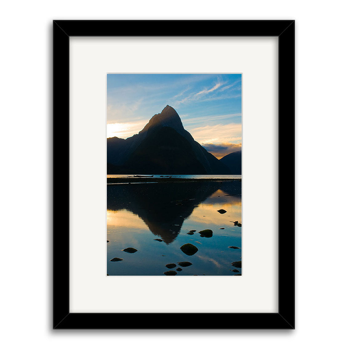 Framed photograph Mitre Peak - RP160 shows a New Zealand mountain reflected in still water at sunrise or sunset, with rocks in the foreground and a partly cloudy sky. Available as archival quality matte photographic prints.
