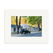 Arrowtown in Autumn - RP162: A vintage black car on a tranquil, tree-lined Arrowtown street, set against historic buildings and clear skies—captured as a photographic print on archival matte paper, perfect for NZ art lovers.