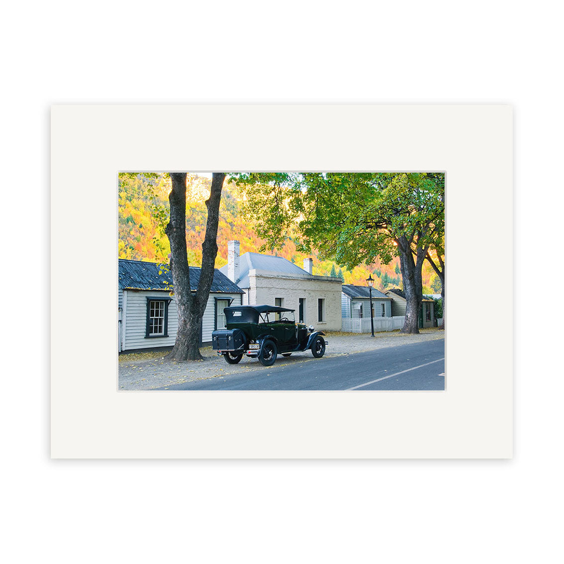 Arrowtown in Autumn - RP162: A vintage black car on a tranquil, tree-lined Arrowtown street, set against historic buildings and clear skies—captured as a photographic print on archival matte paper, perfect for NZ art lovers.