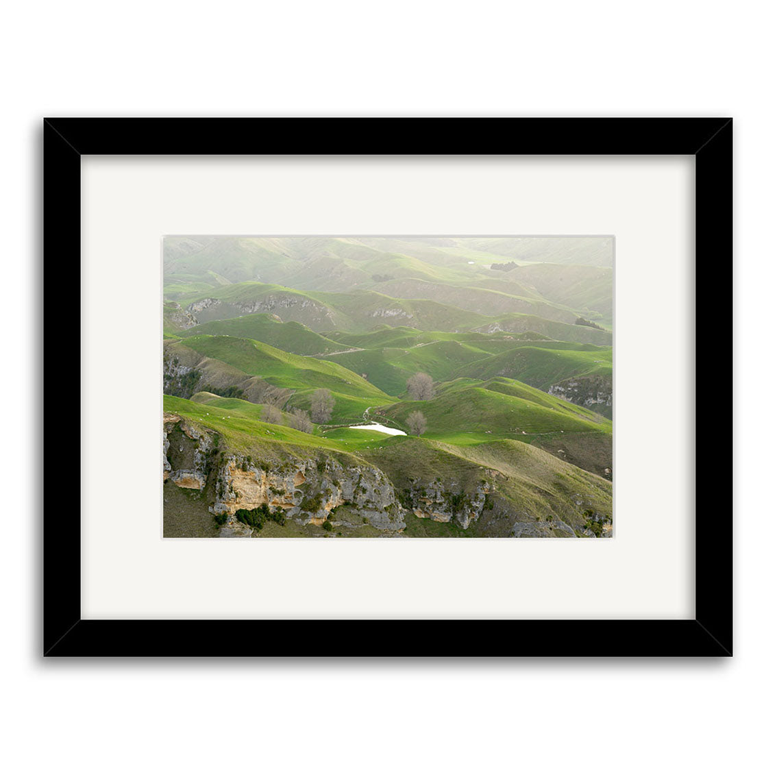 View from Te Mata - RP166: A black-framed, white-matted archival matte print shows New Zealand’s rolling green hills, a small pond, and rocky outcrops.