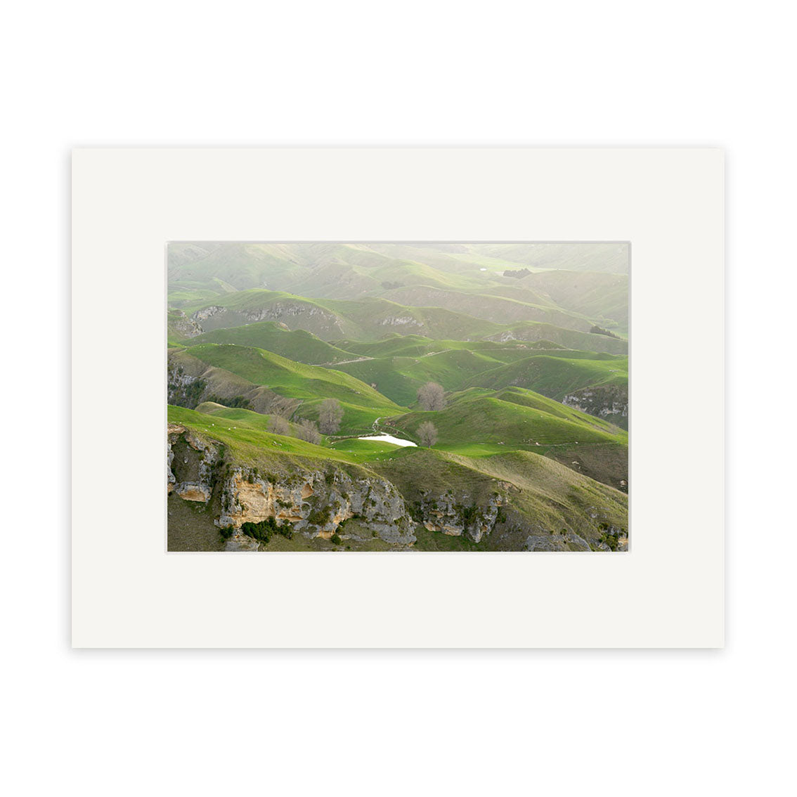 View from Te Mata - RP166: A serene framed photograph of New Zealand’s green hills with rocky patches and a pond beneath a cloudy sky, printed on archival quality matte paper—perfect for fine photographic displays.