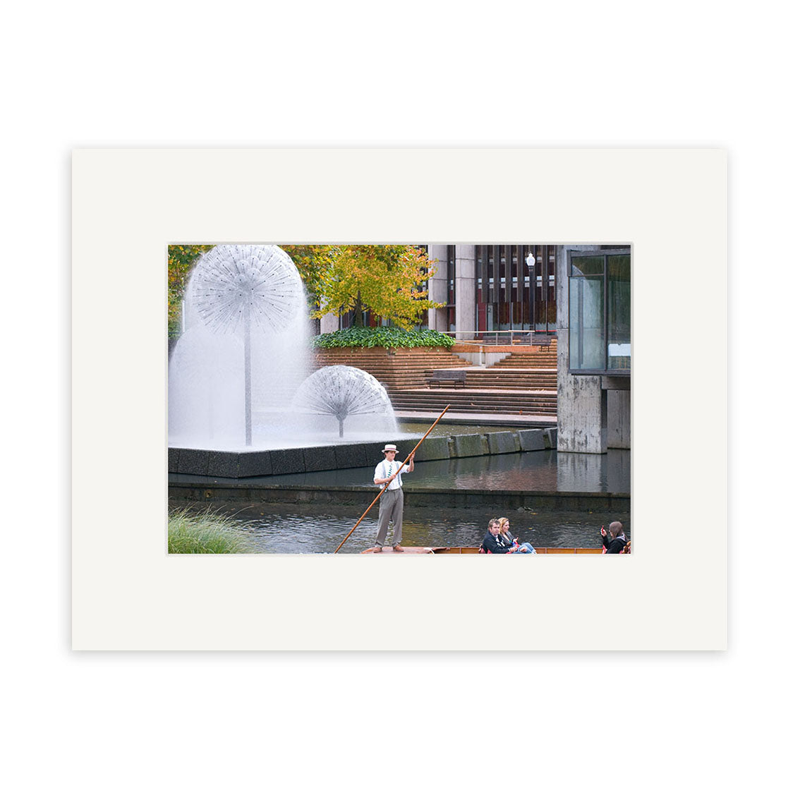 Punting on Avon River - RP171: A man poles a punt with passengers along New Zealand’s Avon River, passing modern buildings, green trees, and dandelion-shaped fountains—ideal for photographic prints on archival quality matte paper.