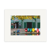 Photographic prints of Antigua Boat Sheds - RP172 capture a row of colorful kayaks and canoes along a calm New Zealand waterfront, with the iconic green-and-white striped shed in the background.