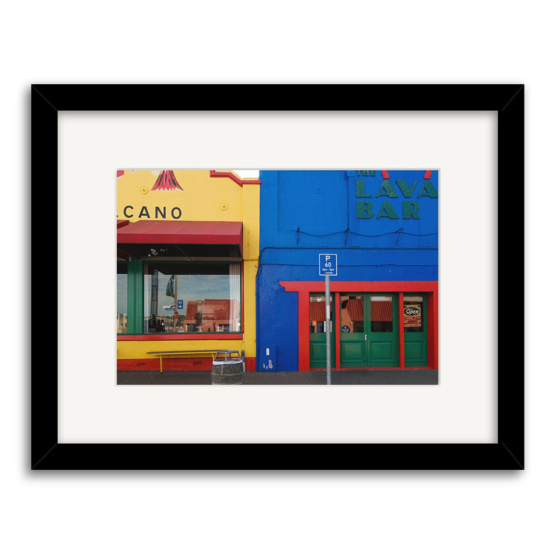 The Lyttelton - RP173 is a framed photographic print on archival paper featuring two adjacent storefronts—one yellow labeled CANO, one blue marked LAVA BAR—with a green door, red trim, windows, and a blue handicap parking sign.