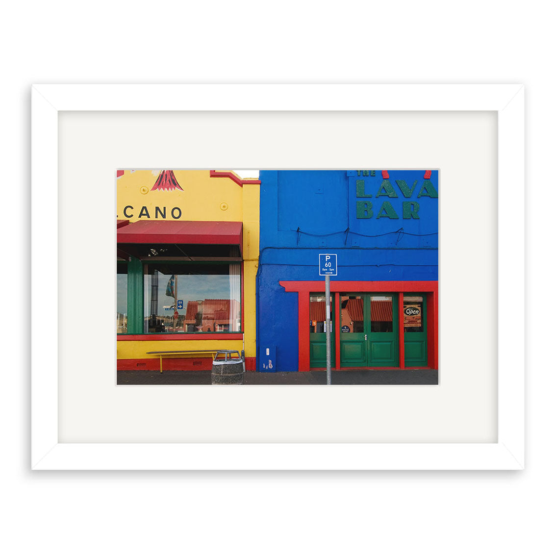 The Lyttelton - RP173 is a framed photographic print of two adjacent storefronts—one yellow labeled CANO, one blue with LAVA BAR, featuring a green door and handicap parking sign. Printed on archival quality paper for lasting vibrancy.
