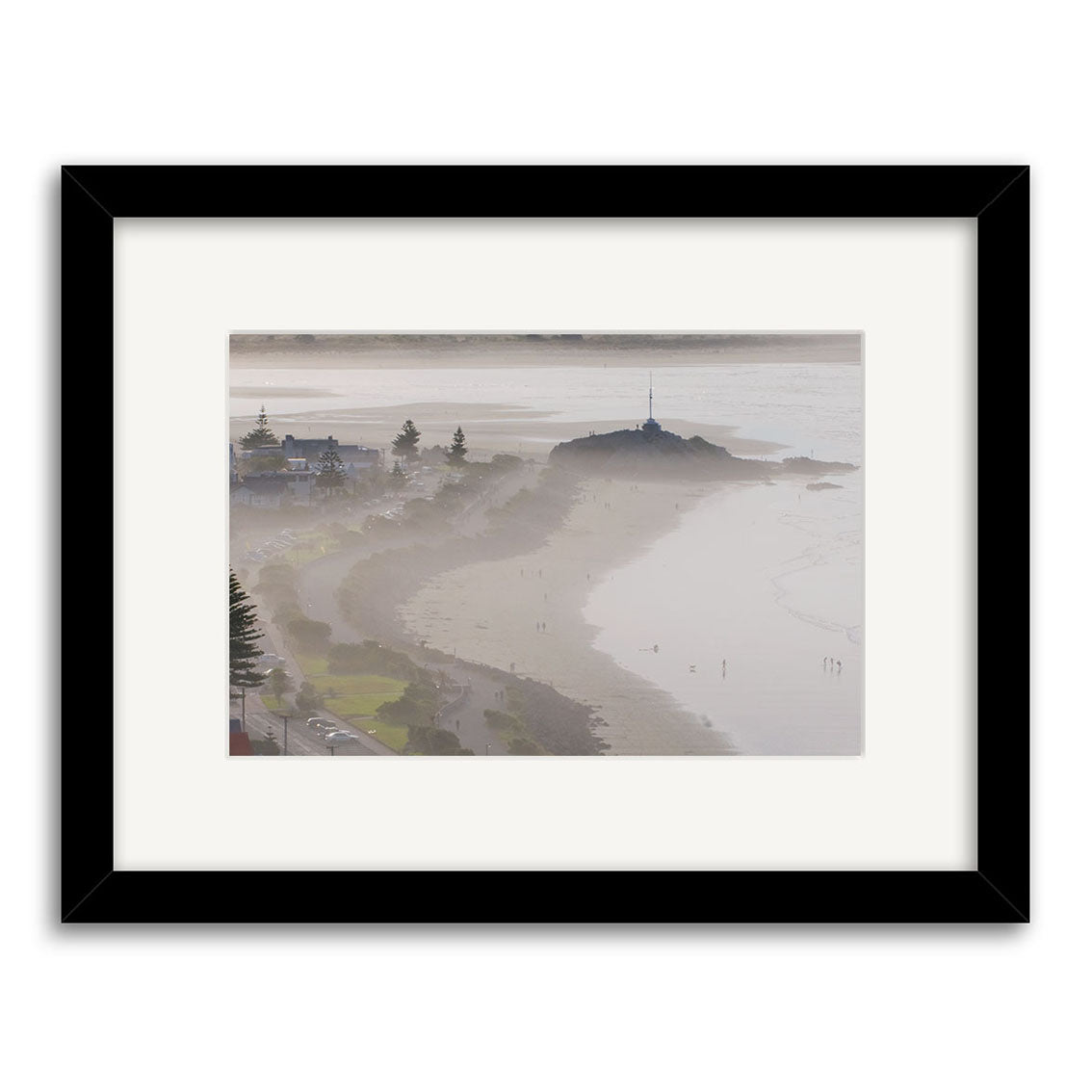 The Sumner - RP174 is a framed photographic print featuring a misty New Zealand beach, shoreline buildings and trees, and a rocky hill with a pole atop, all beautifully printed on archival quality matte paper.