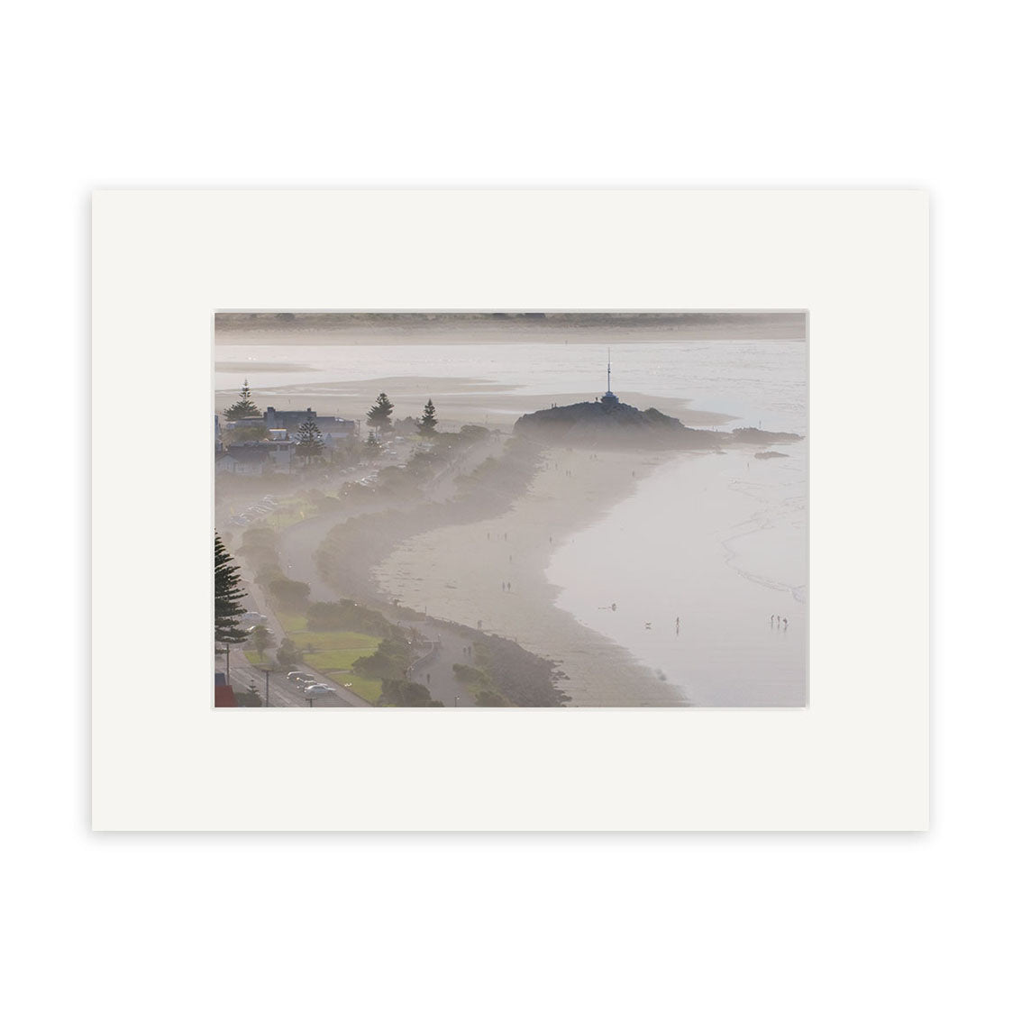 Sumner - RP174: A coastal New Zealand scene with a misty beach, gentle waves, a rocky outcrop with a mast, and buildings and trees along the shore. Archival-quality photographic print on matte paper.