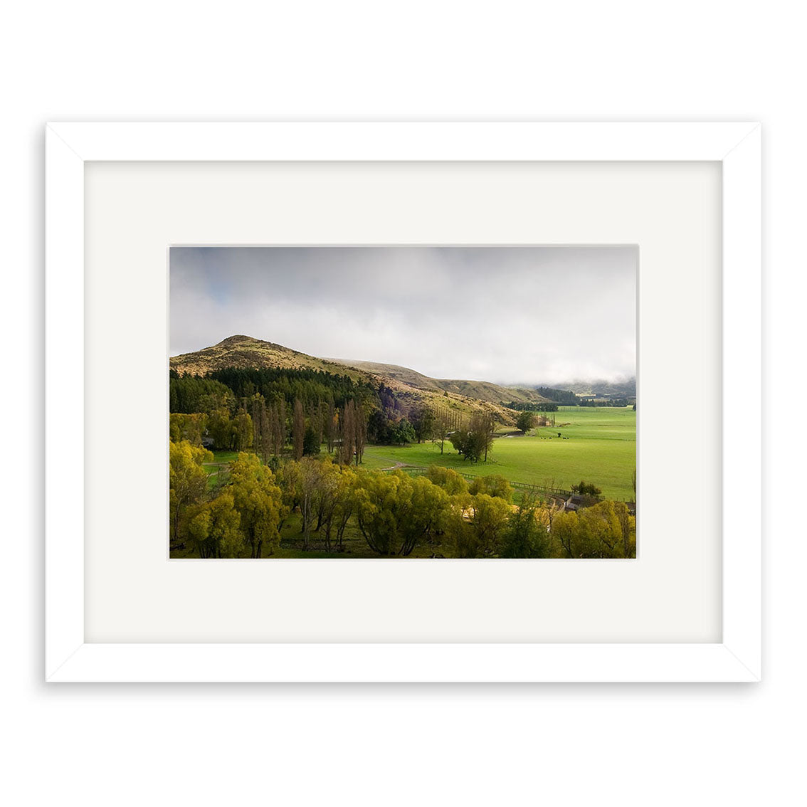 The Inverary Station - RP176 framed photo features green fields, scattered trees, and a hill beneath a cloudy sky. Printed on archival matte paper, it is presented in a white frame with wide matting for an elegant look.
