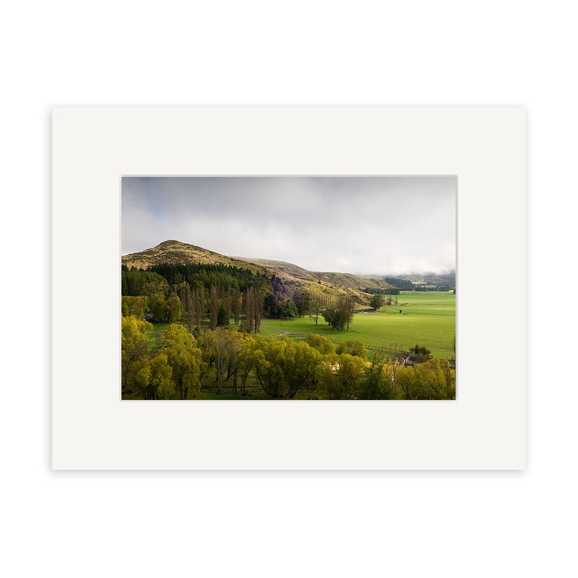 A wide landscape photo of green fields, rolling hills, and scattered trees under a cloudy sky. Inverary Station - RP176 is available as photographic prints on archival quality matte paper with a white mat border.