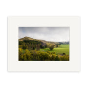 A wide landscape photo of green fields, rolling hills, and scattered trees under a cloudy sky. Inverary Station - RP176 is available as photographic prints on archival quality matte paper with a white mat border.