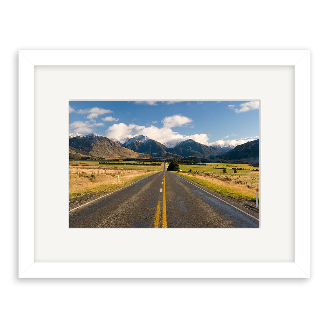 A paved road leads to distant mountains beneath a partly cloudy sky in this photographic print, Arthurs Pass - RP177. Elegantly framed with a white mat, it features archival quality matte paper for lasting beauty.