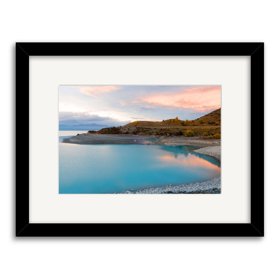 Lake Pukaki - RP178 by Reuben Price: A framed photograph of a serene blue lake and rocky shore beneath pink-orange clouds, printed on archival matte paper with a white mat and black frame. Part of the New Zealand photographic prints collection.