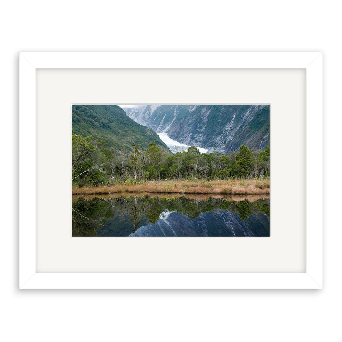 The Franz Josef Glacier - RP181 is a framed photographic print of a scenic New Zealand landscape with dense green trees and glacier, reflected in calm water, printed on archival quality matte paper.
