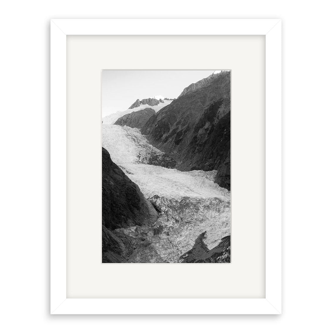 Franz Josef Glacier 1 - RP183: Black and white photo of a glacier amid New Zealand’s rugged peaks, presented in a white mat and frame, printed on archival matte paper for enduring quality.