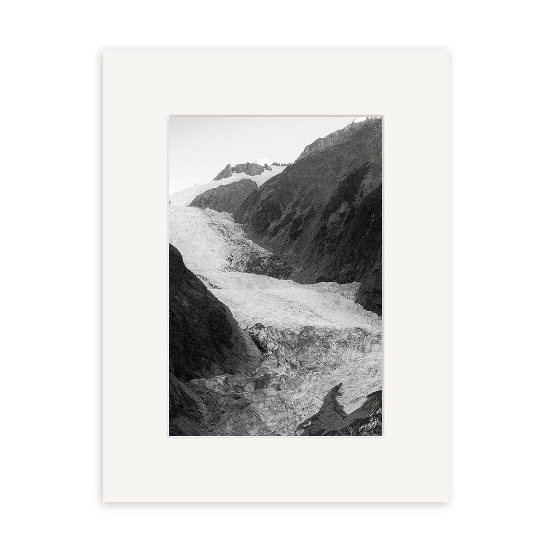 Franz Josef Glacier 1 - RP183: Black and white photo of a glacier amid steep, rocky New Zealand mountains, displayed with a wide white mat. The textured glacier is ideal for prints on archival quality matte paper.