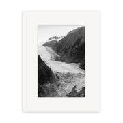 Franz Josef Glacier 1 - RP183: Black and white photo of a glacier amid steep, rocky New Zealand mountains, displayed with a wide white mat. The textured glacier is ideal for prints on archival quality matte paper.