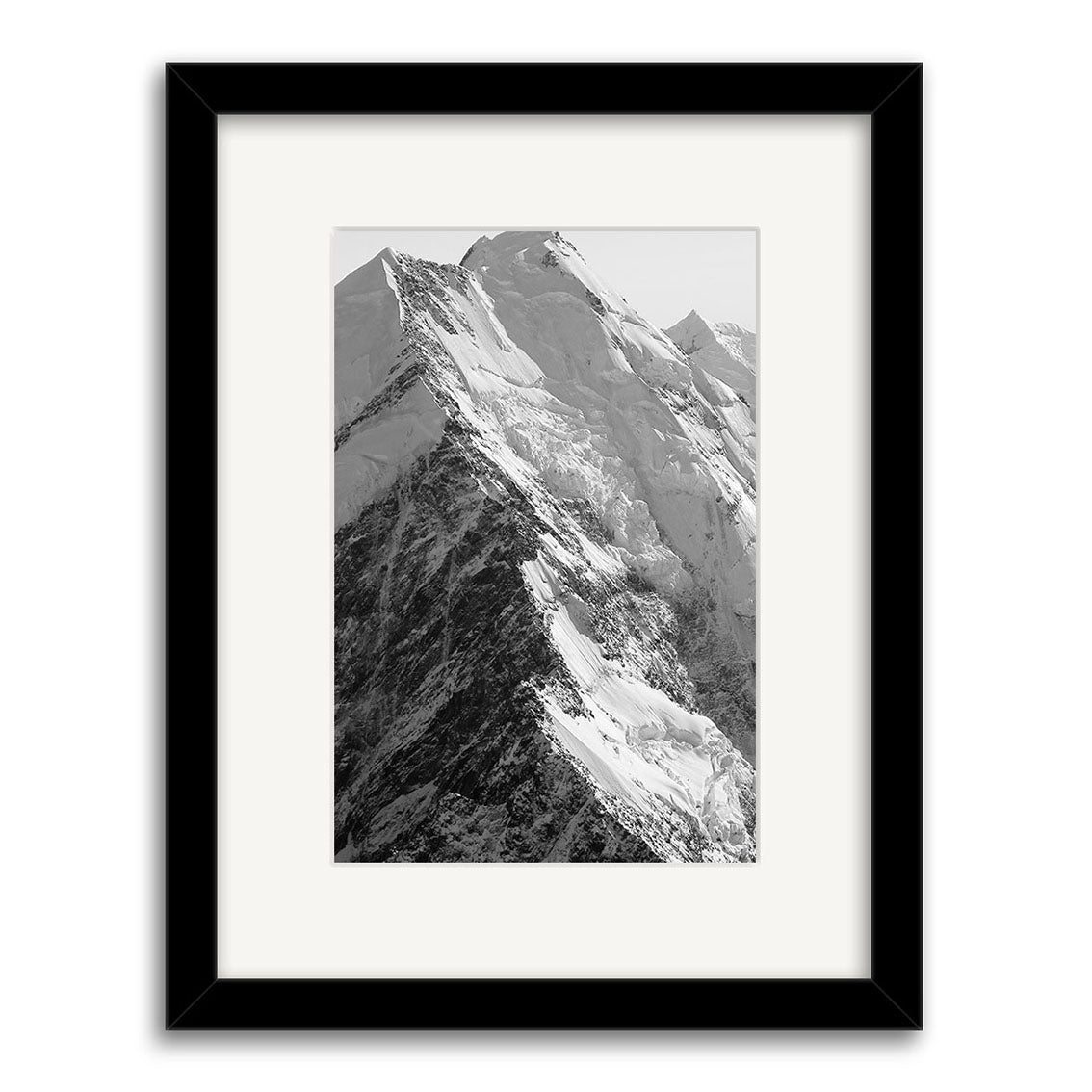 The Mt Cook - RP185 is a black and white photo print by Reuben Price, featuring a snow-covered mountain peak. Printed on archival matte paper, it comes in a black frame with a white mat, accentuating the ridges and texture of the scene.