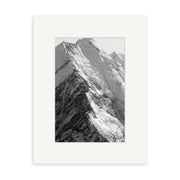 Black and white photograph Mt Cook - RP185 by Reuben Price features a snow-covered mountain peak with sharp ridges, centered in a white mat frame. This New Zealand print is created on archival quality matte paper against a plain white background.