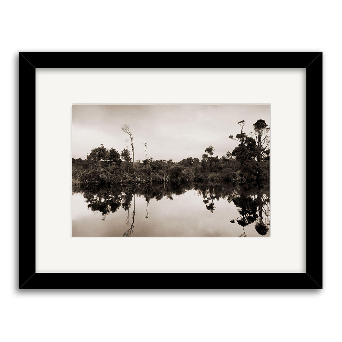Gillespies Beach Reflections - RP189: A framed black-and-white photo of tranquil water mirroring shoreline trees under a cloudy sky, expertly printed on archival matte paper. Inspired by New Zealand’s serene landscapes.
