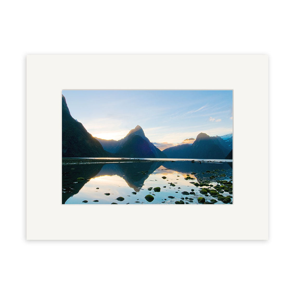 Milford Sound - RP191: A serene lake with rocks, tall mountains, and blue sky reflected in the water. Printed on archival matte paper and displayed with a white mat border.