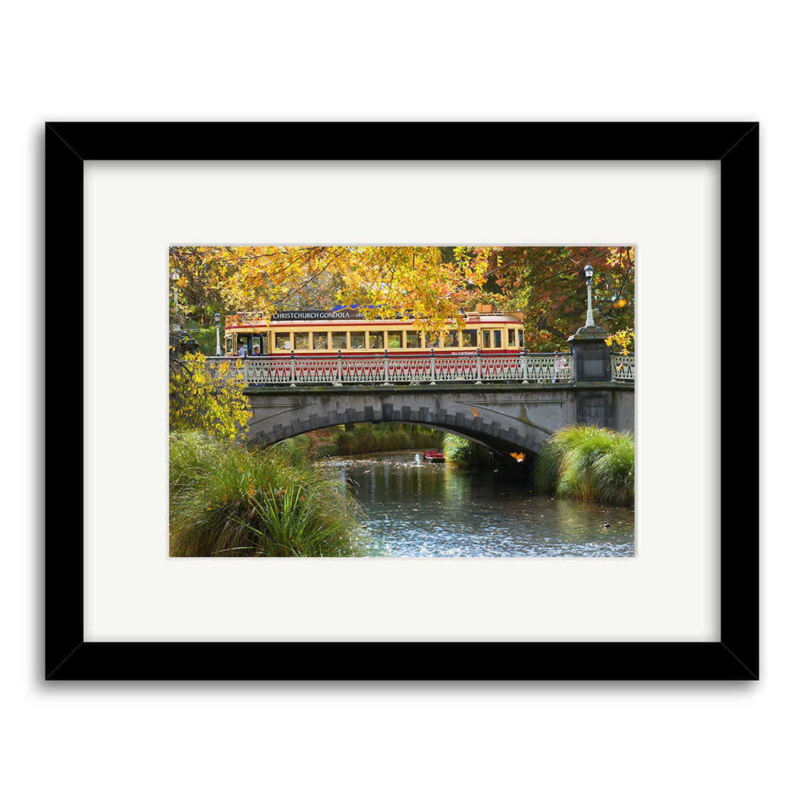 A vintage tram crosses a stone bridge over the Avon River amid autumn trees in this photographic print, titled Avon River - RP192, framed in black with a white mat on archival-quality matte paper.