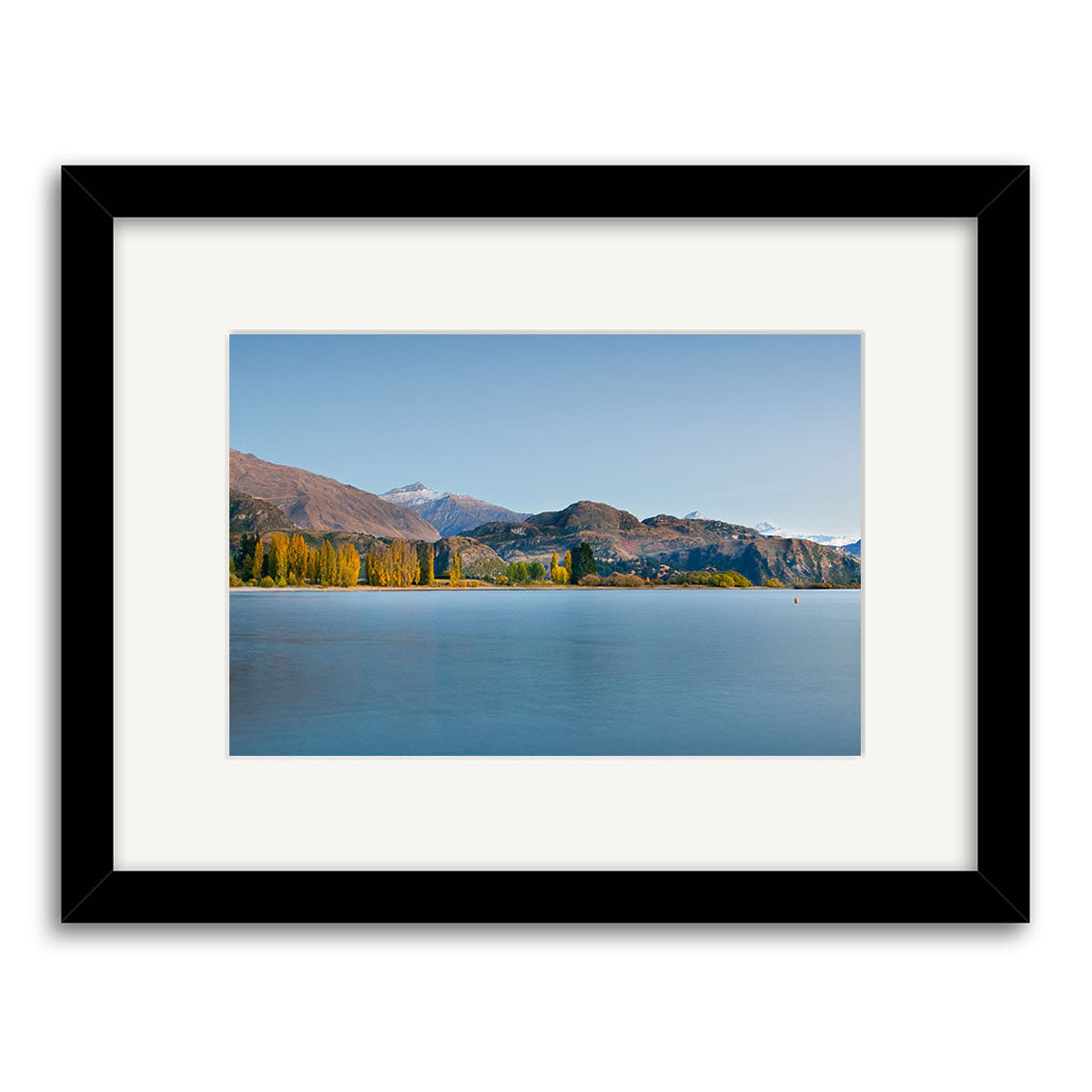 “Lake Wanaka in Autumn – RP193: Framed archival matte print featuring a tranquil New Zealand lake with clear blue water, yellow autumn trees on the shore, and snow-capped mountains in the background.”.