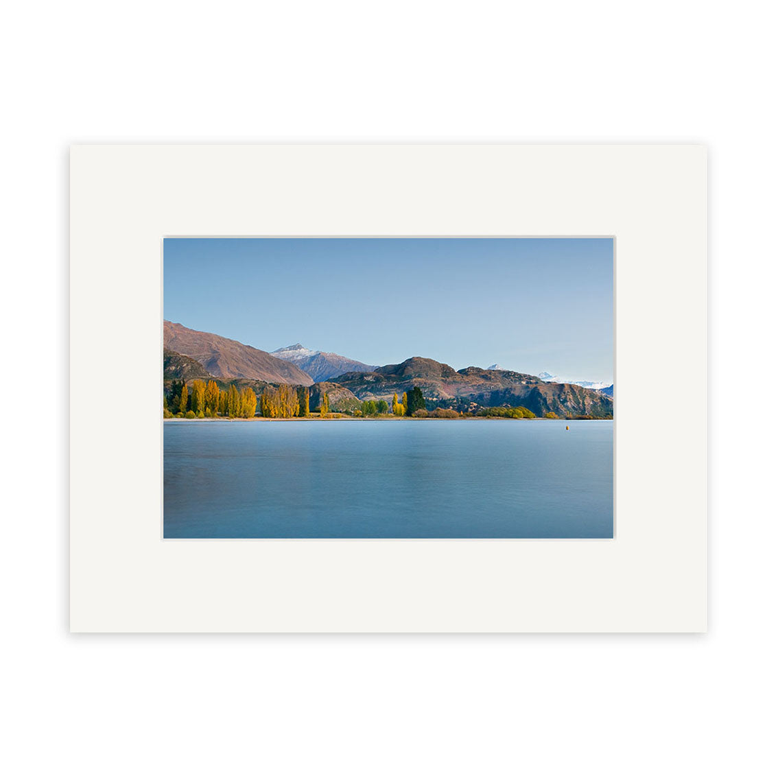 A photograph titled Lake Wanaka in Autumn - RP193 features a calm lake, yellow-leaved trees, and mountains beneath New Zealand’s clear blue sky, printed on archival quality matte paper with a white matte border.