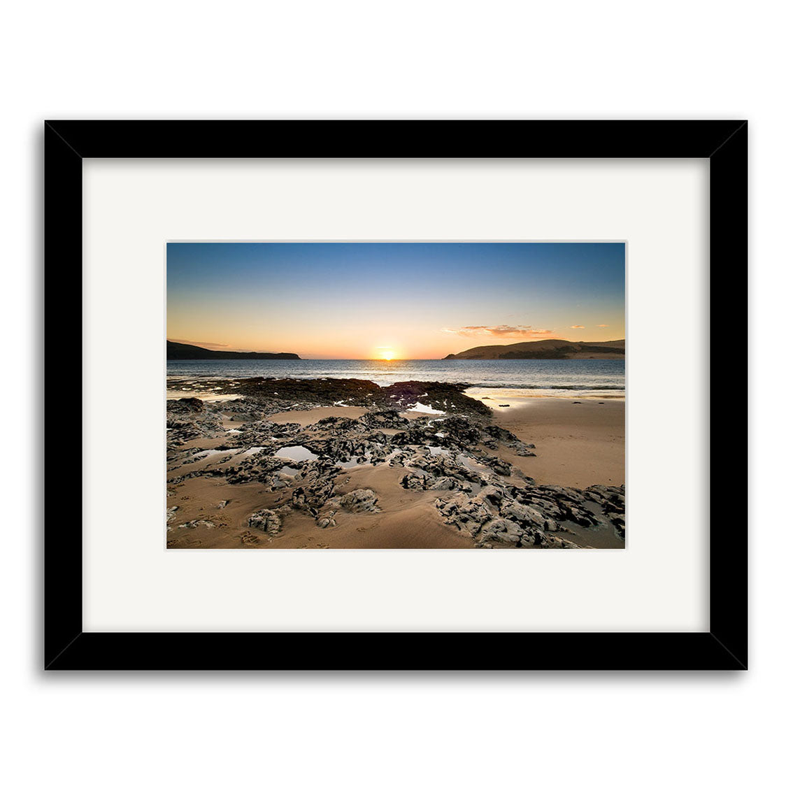 Framed photograph Opononi - RP197 features a New Zealand beach at sunset, rocky foreground, calm water, and distant hills beneath a clear sky. Archival quality photographic prints ensure lasting beauty.