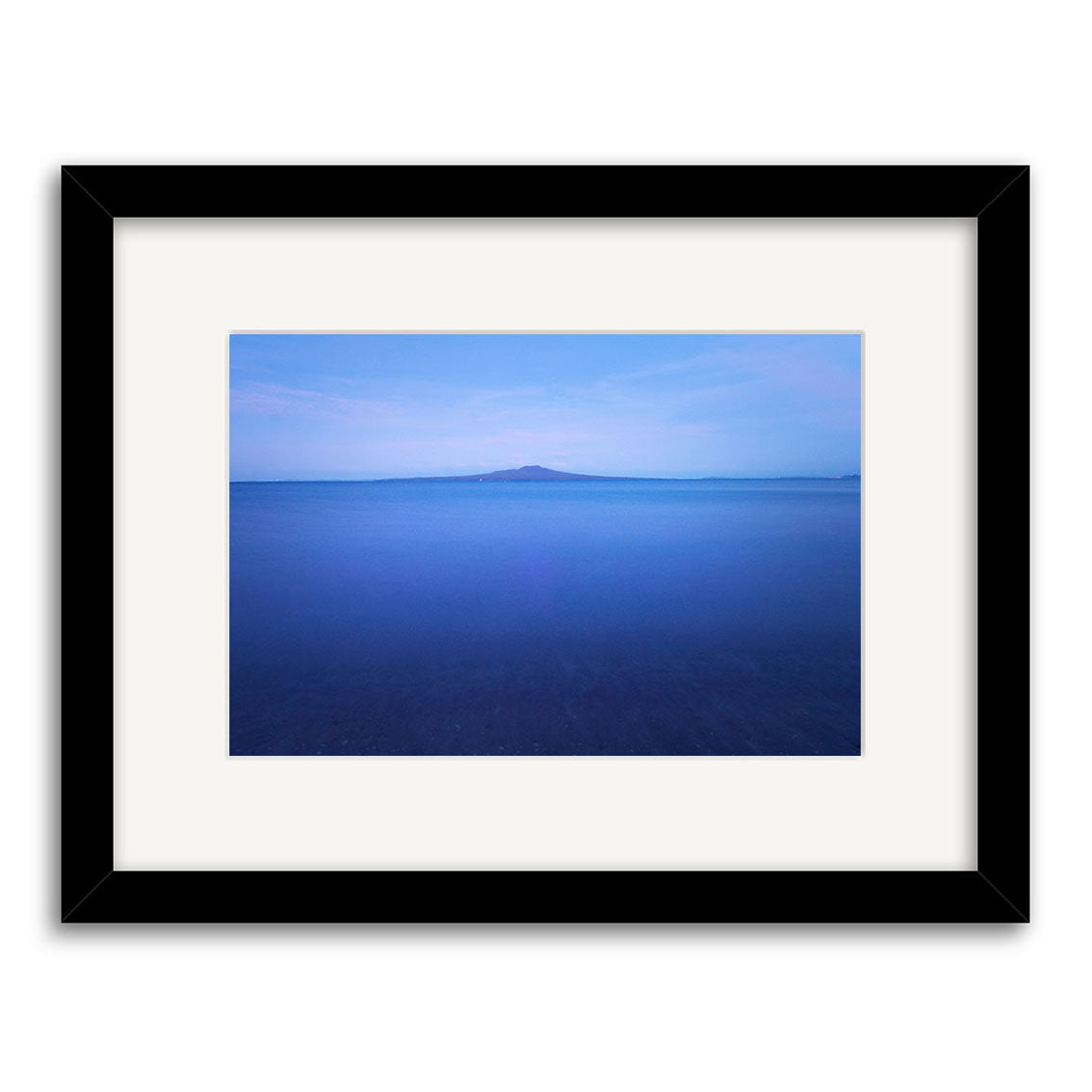 Rangitoto in Moonlight - RP198: An archival-quality photographic print from New Zealand, featuring a calm blue seascape with a distant island under a pale sky, elegantly framed in black with a wide white mat.