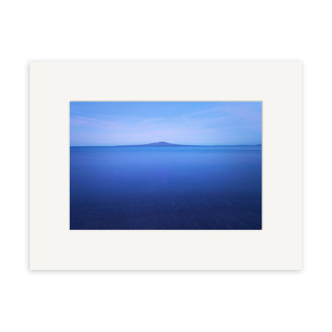Rangitoto in Moonlight - RP198: A framed photographic print of a calm, blue New Zealand seascape under a clear sky, featuring a distant island. Image is centered with white mat on archival-quality paper and blank background.
