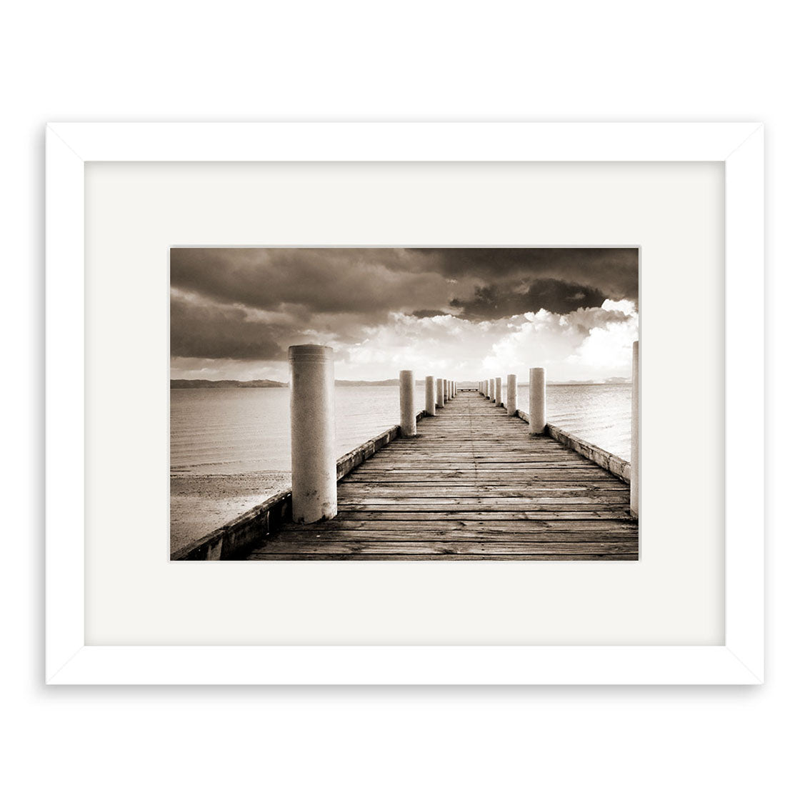Magazine Bay - RP199: Black and white photo of a wooden pier in New Zealand, bordered by white posts and calm water under a cloudy sky. Beautifully framed with a white mat and frame, printed on archival-quality matte paper.