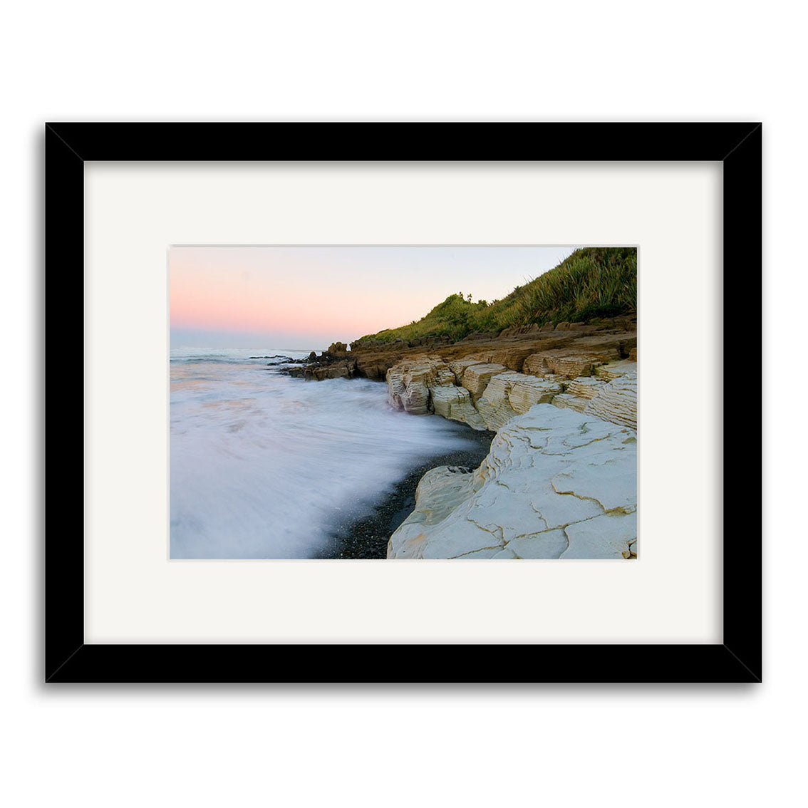 Framed “Punakaiki - RP201” features Reuben Price’s stunning photo of a rocky shoreline, ocean waves, lush hillsides, and a pastel sky—one of our finest New Zealand photographic prints.