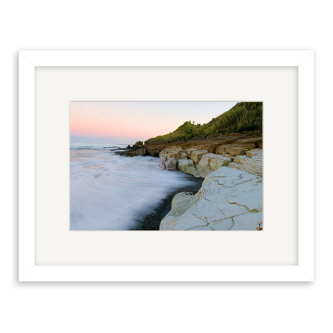 The Punakaiki - RP201 framed photograph features ocean waves over layered rocks, green hills, and a pastel sunset—ideal for those seeking premium New Zealand photographic prints.