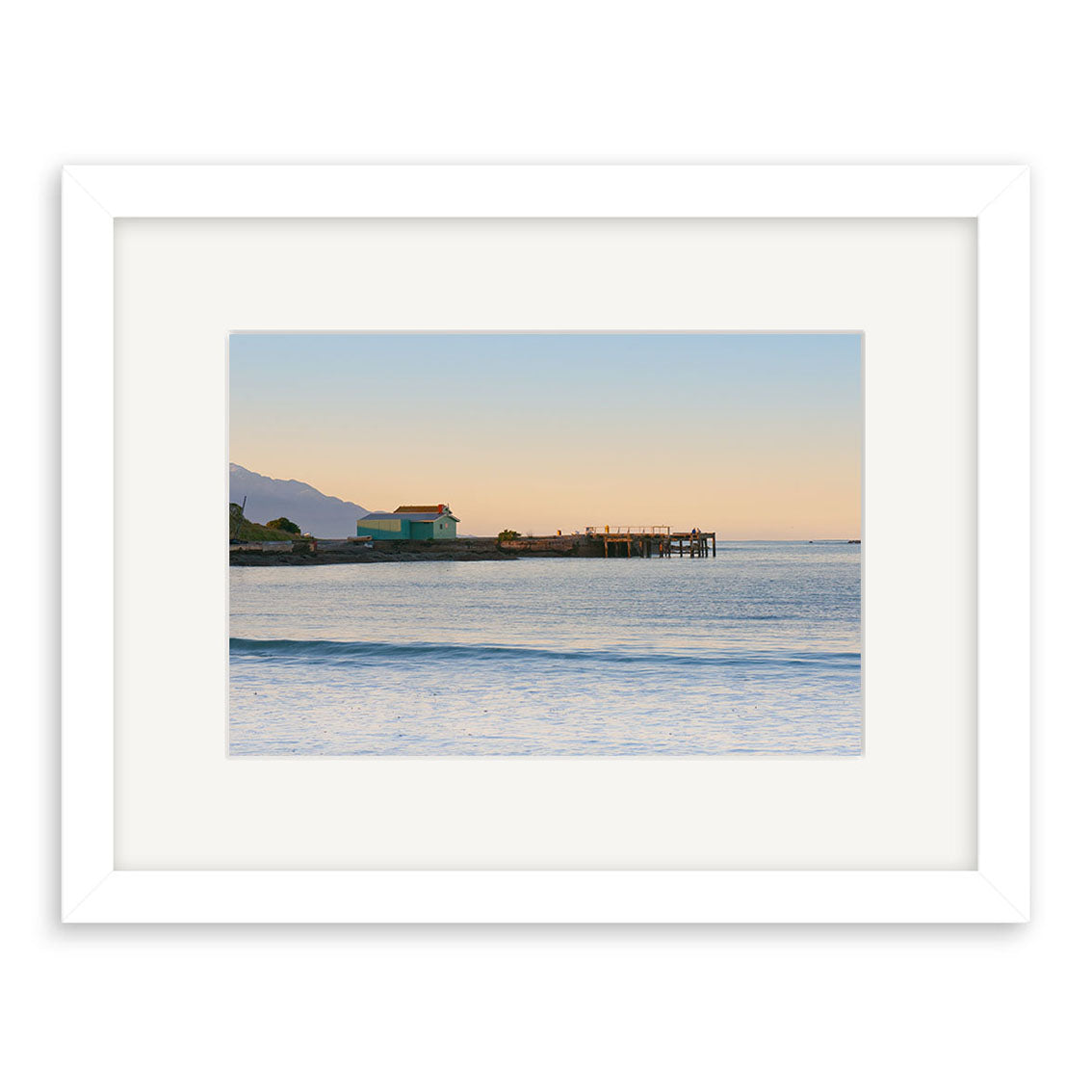 Kaikoura 1 - RP204 is a framed photographic print by Reuben Price, featuring a tranquil sunset ocean scene with a pier, small building, distant mountains, and gentle waves—one of New Zealand’s stunning prints.
