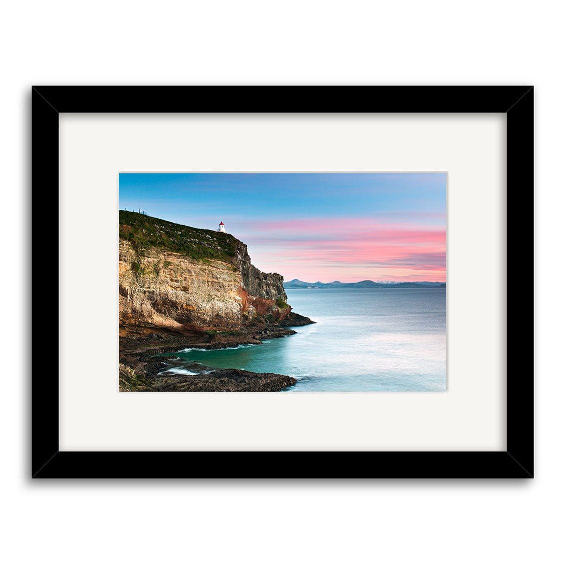 Taiaroa Head Landscape - RP208: A framed photographic print on archival matte paper featuring a rocky New Zealand coastal cliff with a lighthouse, calm blue water, pink and blue sky, and distant mountains.