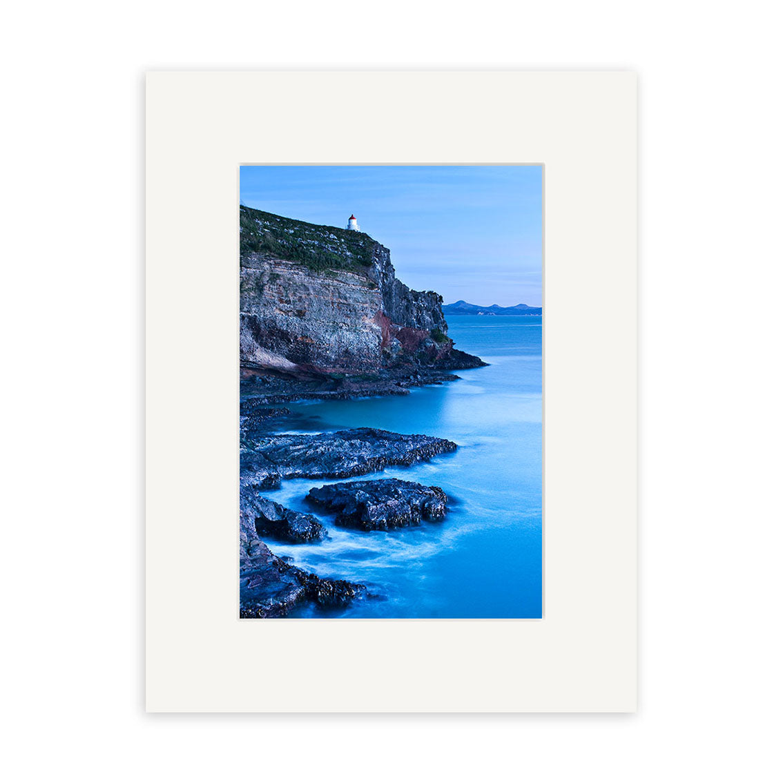The Taiaroa Head Portrait - RP209 features a small lighthouse on a rocky cliff above calm blue waters near New Zealand, distant land visible beneath a clear sky. Available as photographic prints on archival matte paper.
