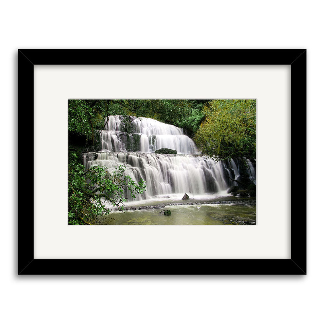 Purakaunui Caitlins - RP216: Framed photo of a multi-tiered New Zealand waterfall amidst lush foliage, water cascading over rocks into a calm pool. Printed on archival matte paper, set in a black frame with white mat.