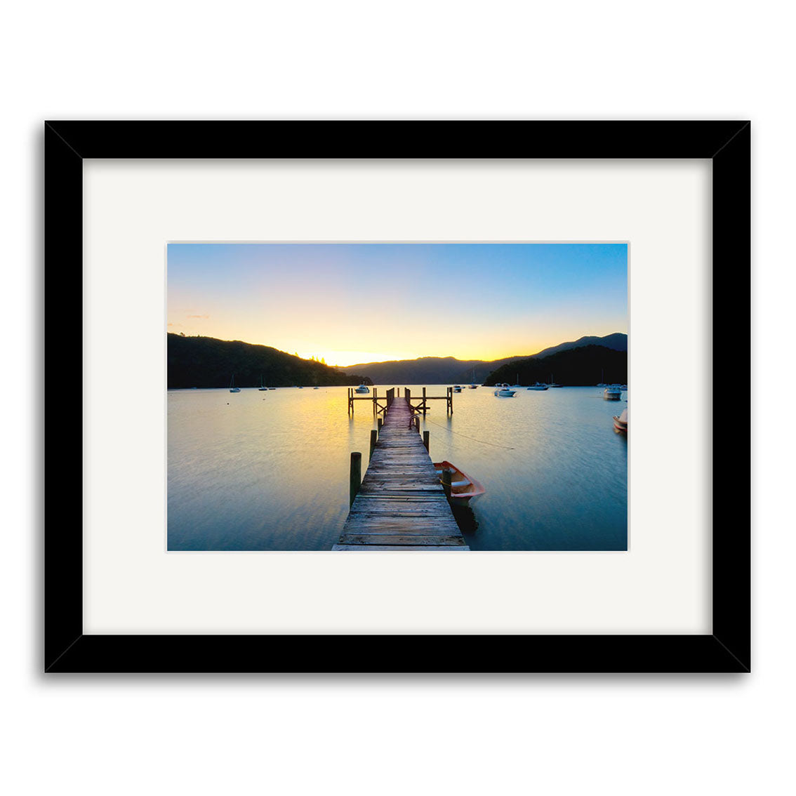 Framed photo Marlborough Sounds - RP220: A wooden dock extends into calm sunset waters in New Zealand, silhouetted hills in the background and boats nearby, printed on archival quality matte paper.