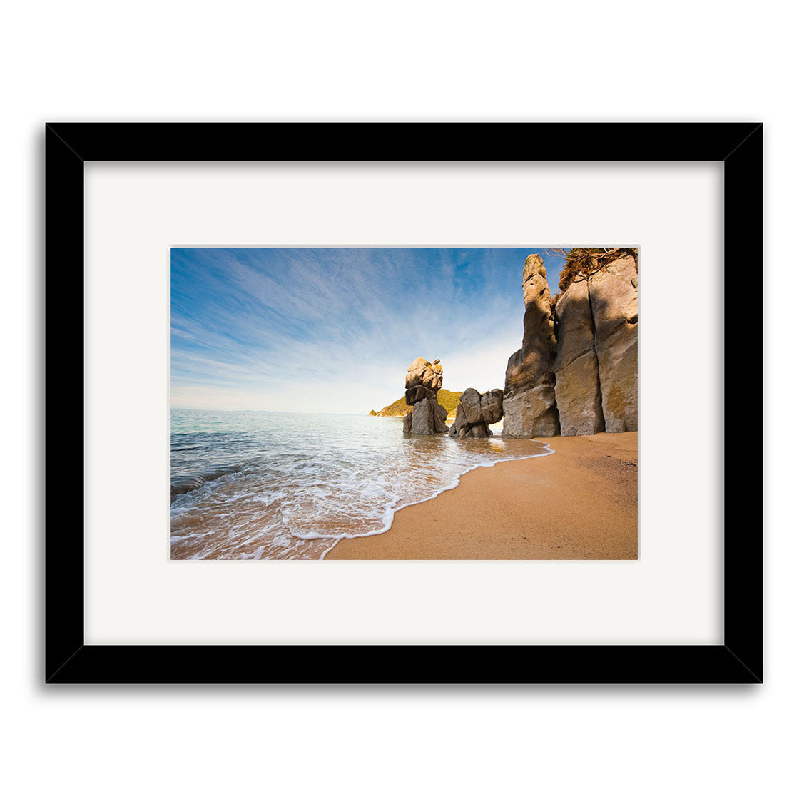 Anapai Bay - RP223 features a framed archival matte photo of a sandy beach, gentle waves, tall rock formations, and a blue sky. The image is presented in a black frame with white mat.