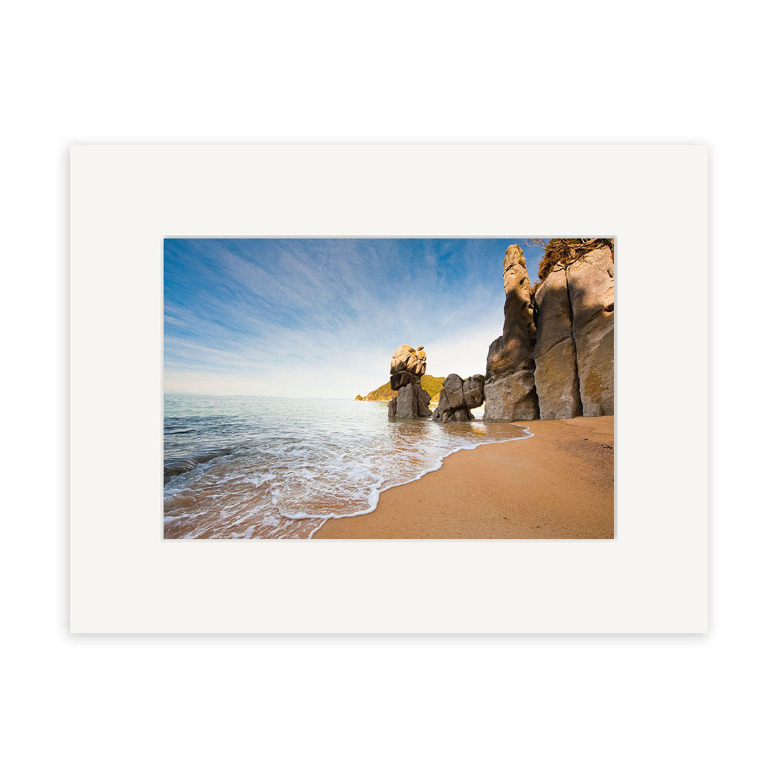 Anapai Bay - RP223: A sandy beach with gentle waves and tall rocky formations beneath a blue sky. This New Zealand scene comes matted in white and is available as photographic prints on archival-quality matte paper.