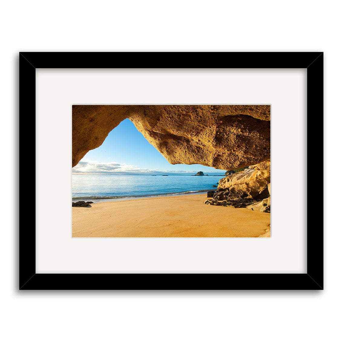 Kaiteriteri Cave - RP224: A framed photographic print of a sandy New Zealand beach from inside a rocky cave, with calm ocean waters and a blue sky, beautifully printed on archival quality matte paper.